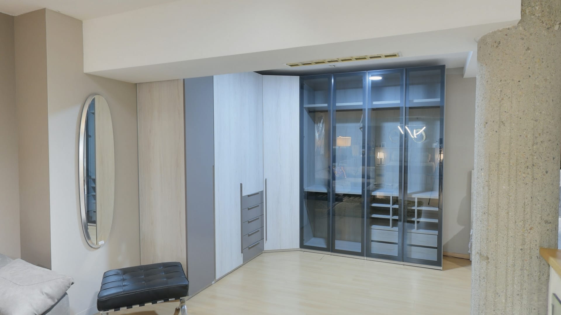 Tienda de Muebles en Barcelona, mobiliario a medida y diseño - Temas Mobiliario Armario esquinero a medida con una sección de puertas de cristal oscuro transparente que muestra estantes interiores, junto a módulos de madera clara y cajonera gris